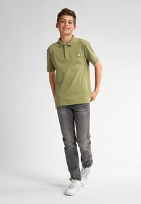 Oliwkowa koszulka polo z kołnierzykiem, z małą naszywką z logo. Połączona z szarymi dżinsami i białymi sneakersami, prezentująca swobodny wygląd.
