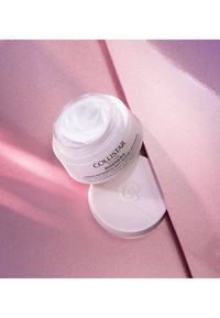 Collistar-krämburk med ett genomskinligt lock som innehåller vit kräm. Burken står på en rosa glänsande yta med subtil textur.