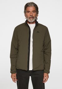 Olivgrön lättviktsjacka med svart dragkedja, hög krage och subtil logo på bröstet. Slen yta och minimalistisk design.