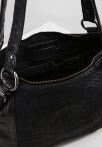 Černá kožená kabelka s texturovaným povrchem, pevnými rukojetmi a zipovým zapínáním. Vnitřek obsahuje kapsy na zasunutí a na zip.