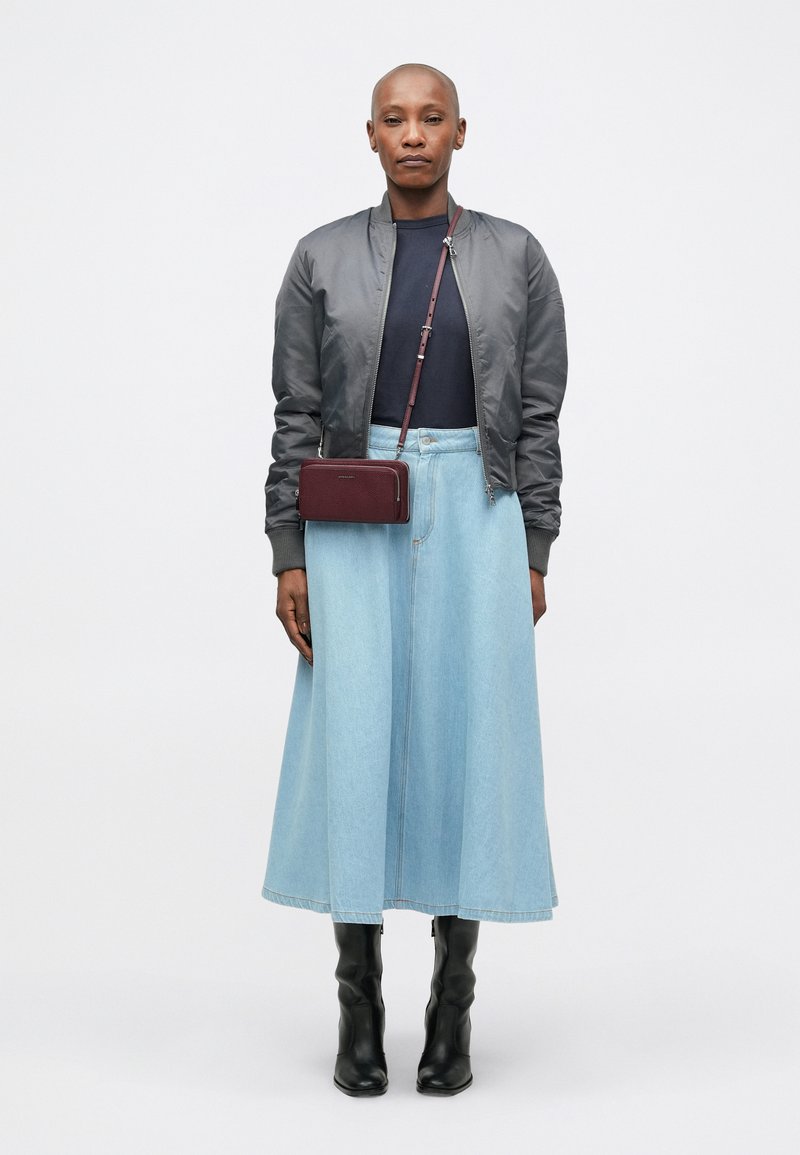 Chaqueta bomber gris sobre una camisa azul marino, combinada con una falda de mezclilla azul clara y botas negras hasta la rodilla. Se lleva un bolso cruzado burdeos.