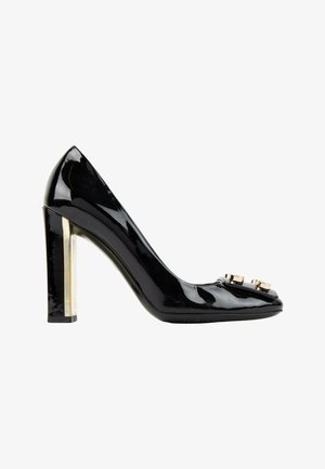 Escarpin en cuir verni noir à talon haut avec un talon bloc métallique doré et deux clous décoratifs dorés sur le bout.