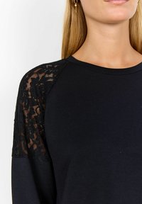 Black long-sleeve top featuring lace accents on the shoulders and a round neckline, made from soft, smooth fabric.