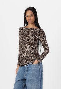 Long-sleeve leopard print top in beige and brown, featuring a boat neckline and slim fit, paired with loose blue denim jeans.