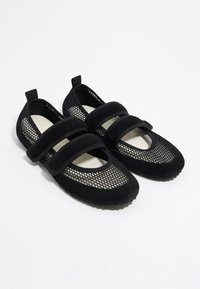 Mustast suedes ja võrgus aluskingad, millel on kaks Velcro rihma, ümarad varbad ja tekstureeritud tallad haardeks.