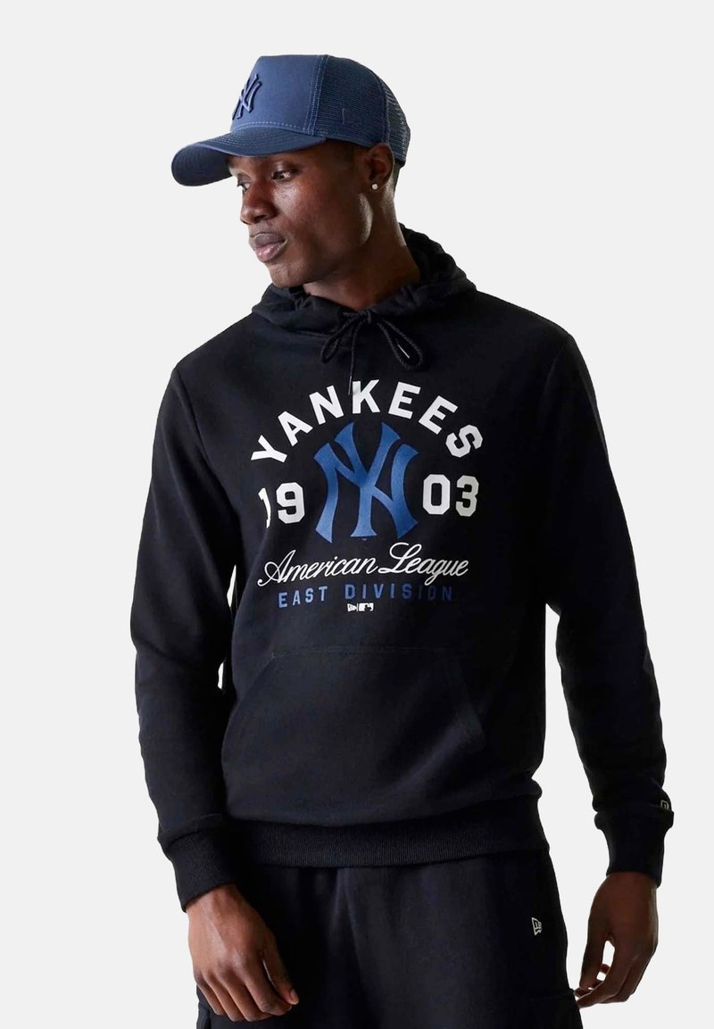 Felpa nera con tasca frontale, con la scritta "Yankees" e altro testo in bianco e blu. Abbinata a un cappellino da baseball blu. Tessuto liscio.
