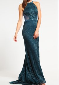Turkusowa sukienka na halter z dopasowanym gorsetem i rozkloszowanym dołem, wykonana z lśniącego, teksturowanego materiału. Posiada boczne wycięcia i koralikowe akcenty.