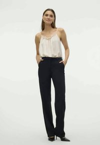 Haut en satin blanc à bretelles avec bordure en dentelle associé à un pantalon noir ajusté. Les deux articles ont une texture lisse et des lignes épurées et soignées.