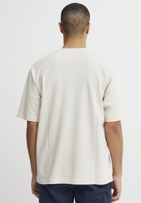 Beige bomull t-skjorte med en avslappet passform, korte ermer og rund hals. Glatt tekstur, minimalistisk design, ingen grafikk eller mønstre synlige.