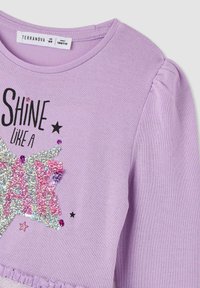 Camicia a maniche lunghe lilla con design a stella in paillettes e il testo "Brilla come una stella", dettagli neri e maniche arricciate.