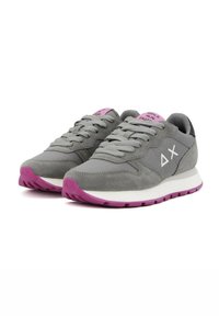 Sneaker sintetiche e in suede grigie con dettagli rosa, lacci piatti e una suola bianca con un motivo a traccia viola. La linguetta include un dettaglio testuale.