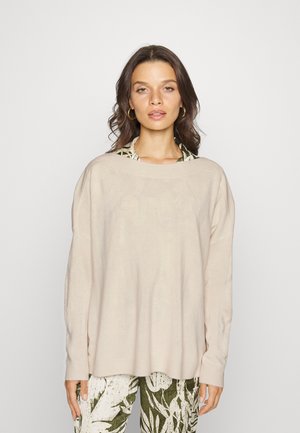 Helle beige Strickpullover mit weiter Boot-Ausschnitt, lockerer Passform, gerippten Bündchen und Saum, kombiniert mit gemusterten grün-weißen Hosen.