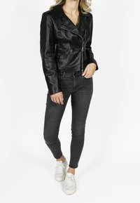 Zwarte leren motorjack met een getailleerd ontwerp, zilveren ritssluiting accenten en revers met inkeping, gecombineerd met donkere jeans en witte sneakers.