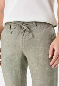 Light green linen pants featuring a drawstring waist, textured fabric, and a relaxed fit, with a button closure and front pockets.