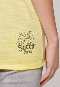 Gelbes T-Shirt mit kurzen Ärmeln und abgerundetem Saum. Verziert mit einem schwarzen Druckdesign, das "Lass uns um 2 Uhr morgens auf einem Dach sitzen. Soccx Geschichten" liest.