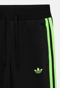 Zwarte joggingbroek met elastische tailleband, voorzien van neonkleurige groene zijstrepen en een klein groen logo op de rechterzak. Zachte textuur.