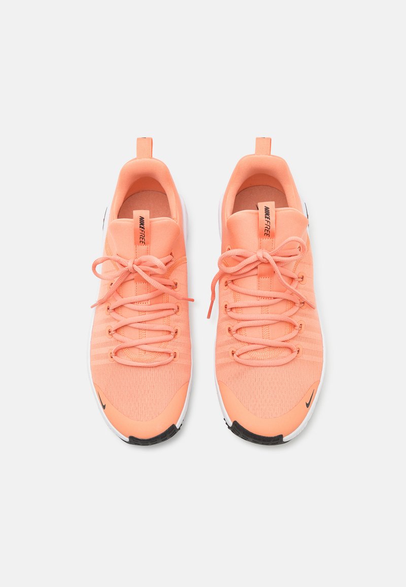 Zapatillas deportivas color durazno con una parte superior de malla texturizada, puntera redonda, cordones en tono y una entresuela blanca con un logo de acento negro.