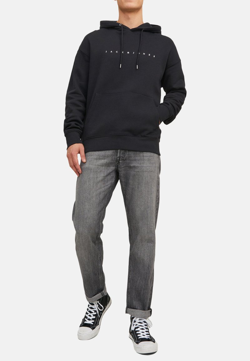 Sort hættejakke med snore og frontlomme, parret med grå jeans og sorte sneakers med hvide såler. Indeholder brandlogo på brystet.
