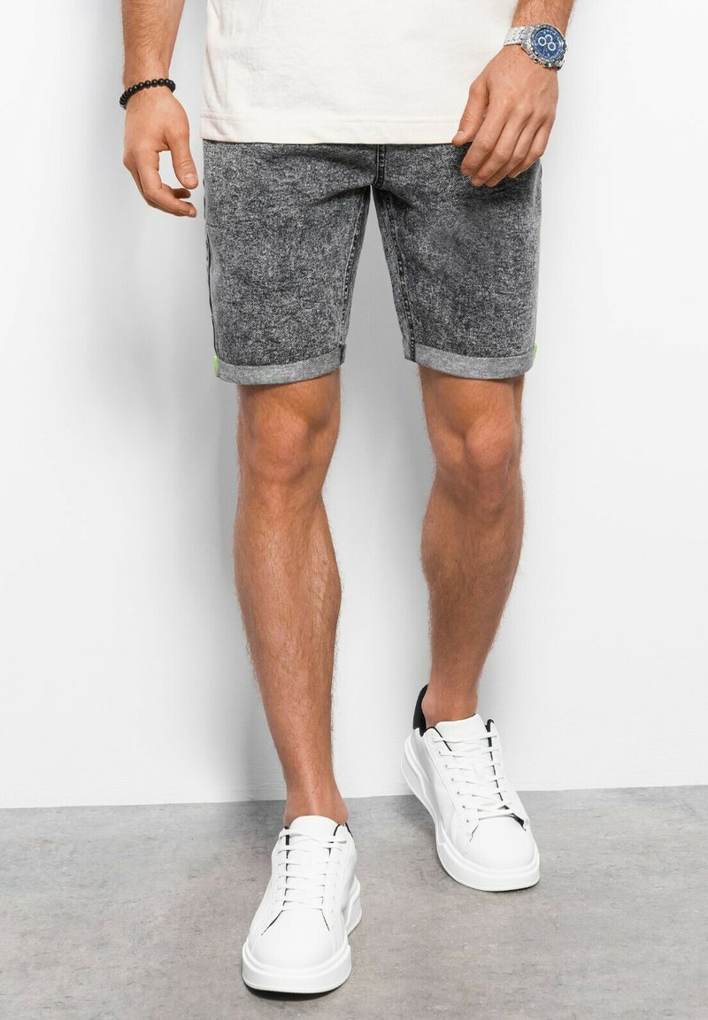 Grijze denim shorts met een opgevouwen zoom, voorzien van een groene accenten. Draagt met witte sneakers, die een casual, hedendaags ontwerp tonen.