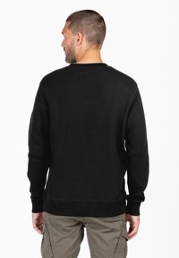 Sudadera negra de cuello redondo con un patrón de tejido texturizado, puños y dobladillo acanalados, vista desde la parte de atrás. Diseño liso, corte casual.
