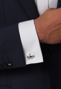 Marines Anzug mit einem weißen Umschlag und einer silbernen Manschette. Die Manschette hat ein strukturiertes zylindrisches Design und wird durch die Knopflöcher des Hemdes gehalten.