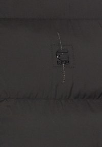 Giacca imbottita nera con finitura lucida, caratterizzata da cuciture a contrasto e una piccola toppa rettangolare con il logo "G-STAR RAW".