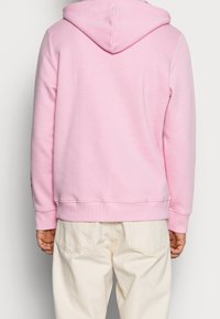 Rosa hoodie i mjukt tyg med en känguruficka och ribbad mudd. På baksidan finns en enkel design utan grafik. Matchad med beige byxor.