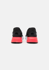 Black and white athletic shoes with a rubber sole. Features a pink accent at the heel and a textured fabric upper with a logo detail.
