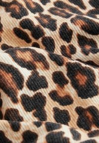 Tkanina s leopardím vzorem a texturovaným povrchem, obsahující černé a hnědé skvrny na béžovém pozadí, tvořící dynamický vzor.