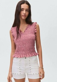 Top rosa con volant, dalla texture arricciata e design a V, abbinato a pantaloni shorts in denim bianchi con borchie argentate sui lati.