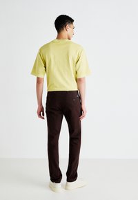 Jasnożółta, krótko rękawowa koszula, brązowe slim-fit spodnie i białe sportowe buty. Prosty design, miękka tekstura i swobodny krój.