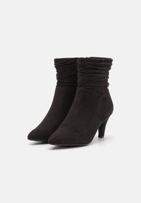 Černé kotníkové boty vyrobené z měkké semišové kůže, s designem shromážděného svršku a špičatou špičkou; přibližně 3palcový jehlový podpatek.