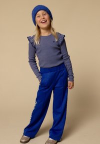 Blauwe gebreide muts en gestreepte longsleeve top met gerimpelde schouders, gecombineerd met blauwe wijde broek. Grijze sportschoenen inbegrepen.