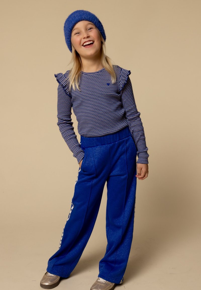 Blauwe gebreide muts en gestreepte longsleeve top met gerimpelde schouders, gecombineerd met blauwe wijde broek. Grijze sportschoenen inbegrepen.