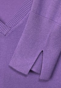 Pull en tricot violet avec col en V et poignets côtelés comportant un trou pour le pouce sur la manche.