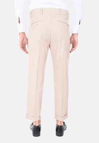Pantaloni beige su misura a gamba dritta, con due tasche posteriori e pieghe discrete. Con orli a fondo, abbinati a scarpe nere.