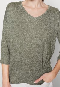 Pull léger vert olive avec col en V, manches trois-quarts, motif tricoté texturé, présentant une coupe décontractée.