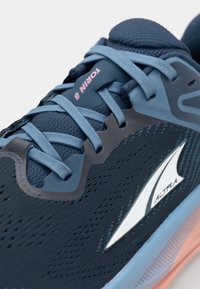 Chaussure de course bleu et marine avec tige en mesh, lacets bleu clair contrastants, logo blanc et semelle intercalaire en pastel rose et bleu.