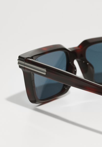 Sunglasses with a tortoiseshell frame, dark blue lenses, and silver accents on the hinges. Square shape with a glossy finish.