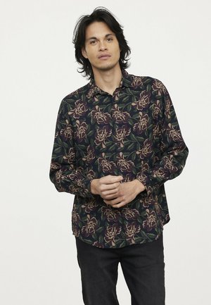 Chemise florale avec un fond bleu marine foncé, ornée de grands motifs de fleurs violettes et vertes complexes, à manches longues et avec un design à boutons.