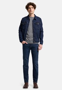 Denimjacke in dunkelblau mit helleren Taschen, grauer Pullover mit Rundhalsausschnitt, eng anliegende dunkle Jeans, braune Schnürschuhe, lässiger Stil, feste Texturen.