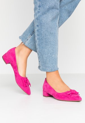 Chaussures en daim rose à petit talon avec un nœud décoratif à l'avant, associées à un jean denim bleu clair raccourci.
