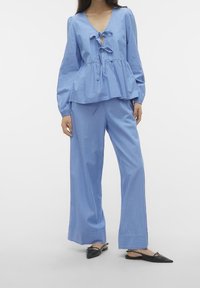 Light blue, striped, long-sleeve top with a V-neck and tie detail; paired with loose-fitting, striped pants. Worn with black pointed flats.