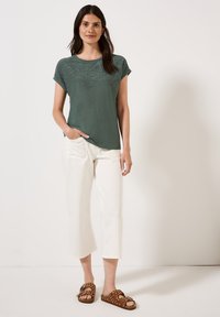 Haut vert à manches courtes avec un design texturé, associé à un pantalon blanc cropped et des sandales marron à pois avec un accent en nœud.