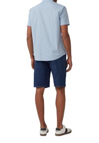 Chemise à manches courtes à carreaux bleu clair associée à un short en denim noir et des baskets blanches avec des accents bruns. Look décontracté, motifs visibles.