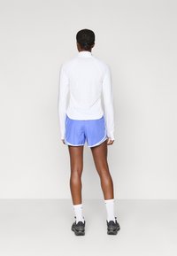 Αθλητική εμφάνιση με λευκή μπλούζα μακρύ μανίκι και μπλε σορτσάκι με λευκές λεπτομέρειες. Μαύρα αθλητικά παπούτσια και λευκές κάλτσες συμπληρώνουν την εμφάνιση.