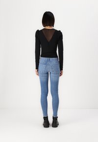 Top negro de manga larga con espalda transparente, combinado con jeans skinny azules y botas negras de tobillo, presentado sobre un fondo blanco liso.