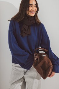 Blue knitted sweater with wide sleeves, paired with a dark brown scarf and a brown suede handbag featuring a zipper and short handles.