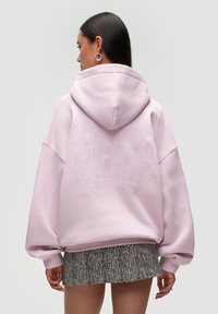 Felpa oversize rosa con un logo testurizzato sul retro, realizzata in un mix di tessuti e con una finitura morbida e liscia. La felpa ha una vestibilità ampia.