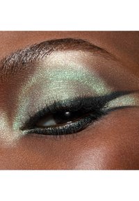 Nærbilde av et øye med glitrende grønn øyenskygge, mørk eyeliner og lange vipper, satt mot en varm hudtone med jevn tekstur.